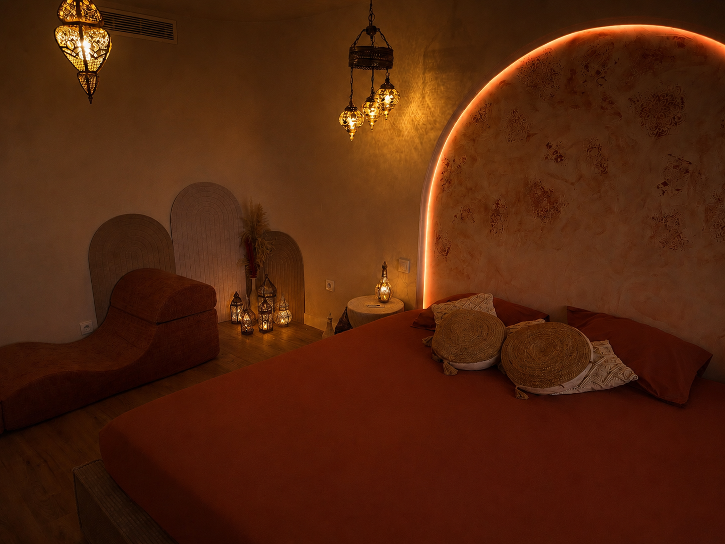 Lit king size sous l'arche lumineuse en tadelakt terracotta, sofa tantrique et lanternes marocaines — riad oriental Secret d'Orient